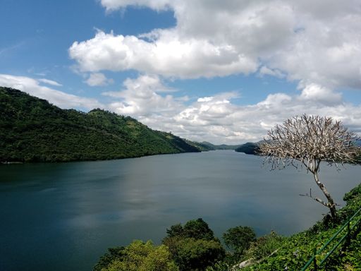 A scenic view of a lake surrounded by mountains covered with green forests under a cloudy blue sky