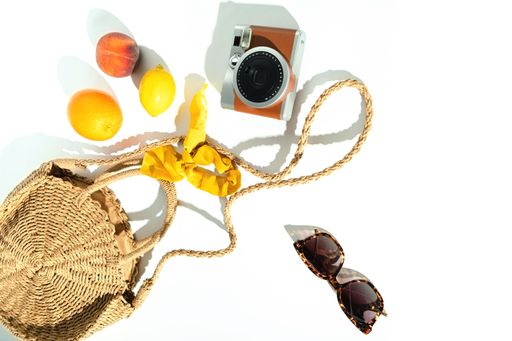 Summer top view with a stray shoulder bag, fruits, sunglasses, scrunchy, and instant camera