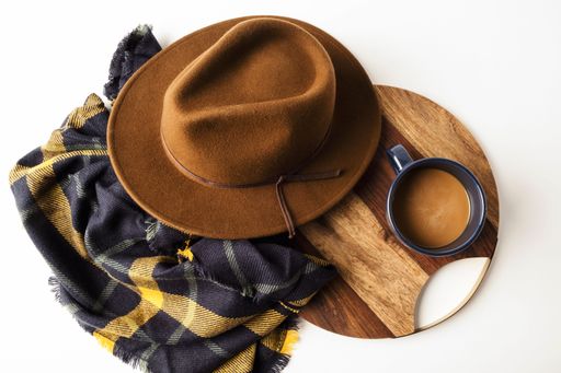Top view of a hat with a cup of coffee on a wooden plate and a beautiful scarf isolated on white background
