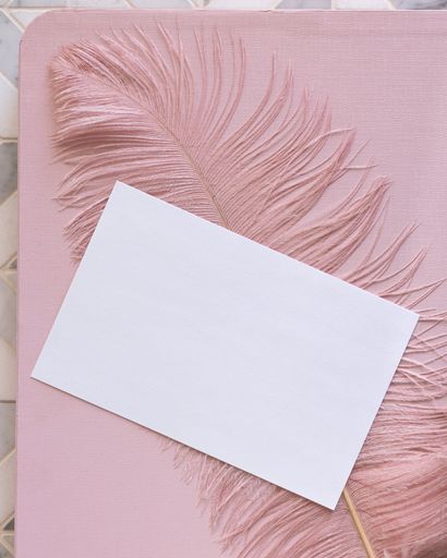 A paper and a feather on a pink surface with copy space