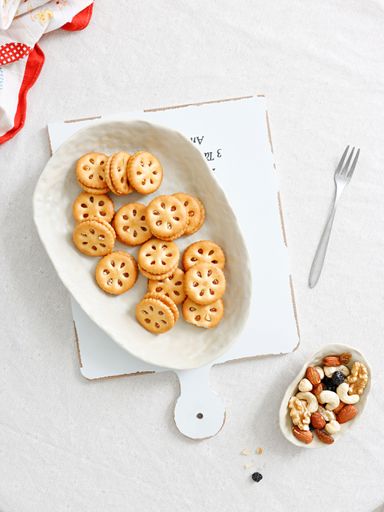 A top view shot of crackers on a white plate and nuts in a smaller bowl