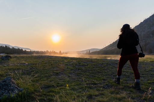 The silhouette of the woman with a camera in Yellowstone National Park at sunrise.