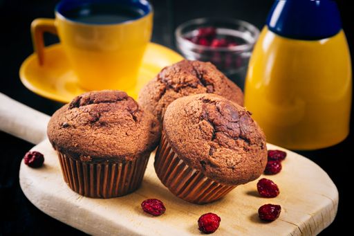 A closeup shot of chocolate cupcakes on a wooden surface with a yellow cup and teapot