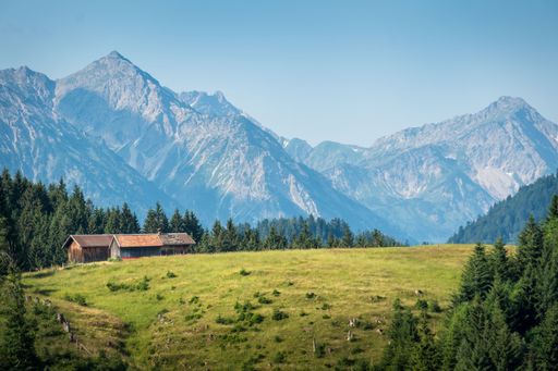 A grassland with farmhouses and high mountains in the background during the daytime