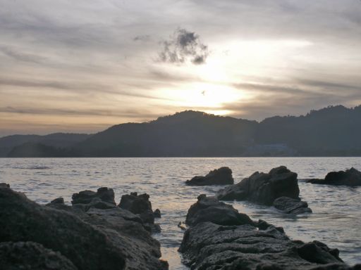 A scenic view of a rocky shore after sunset with mountains visible on the other side