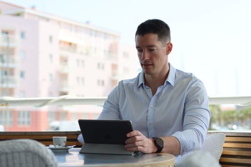 A young man working on his tablet with his coffee and his smartwatch on a terrace of a restaurant