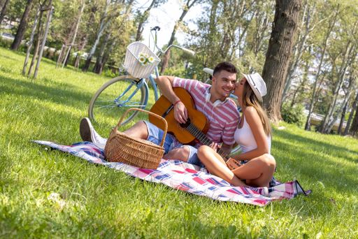 A picture of a beautiful couple with a guitar having a picnic in the park