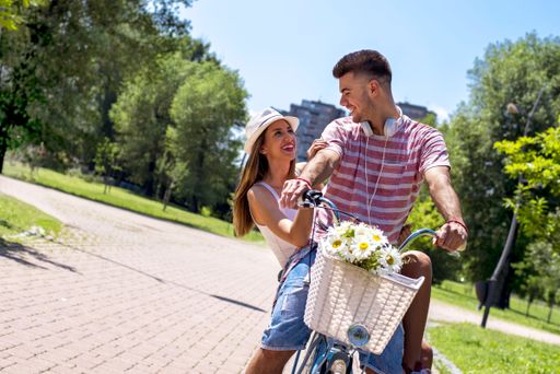 A young Caucasian couple riding a bike in a park during a sunny day