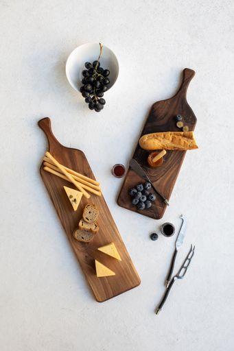 A vertical high angle shot of chopping boards with bread, cheese and berries on a white surface with aesthetic decoration
