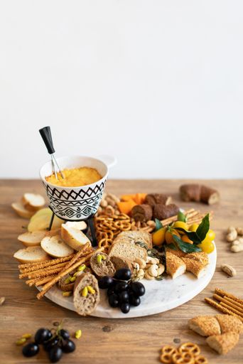 A vertical shot of a breakfast table with different types of cheese, bread, snacks and sauce