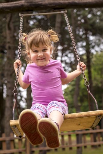 A vertical shallow focus shot of a young female swinging on a swing in playground