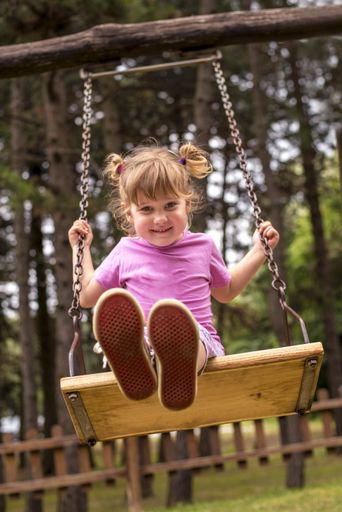 A vertical shot of a happy female child swinging behind the trees