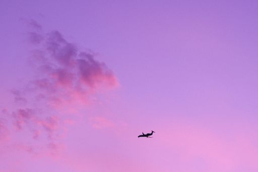 A breathtaking view of a plane flying in the purple sunset sky