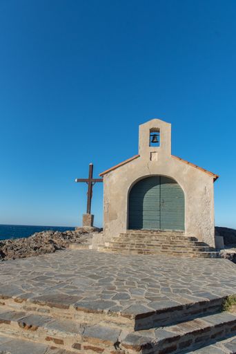 A vertical shot of a small church near a big cross under the sunlight