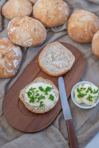 A halved bread roll with cream cheese and chopped greens on a wooden board