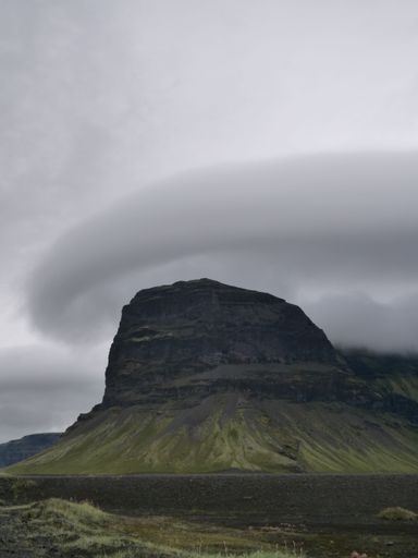 A vertical shot of a green mountain peak against a cloudy sky in Iceland