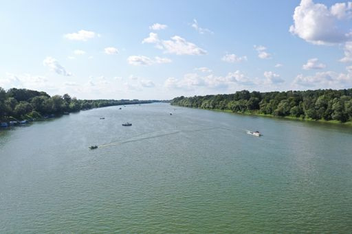 A high angle shot of boats sailing on the river in the middle of trees under a blue cloudy sky in Bosnia and Herzegovina