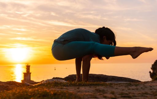 A beautiful Spanish woman doing yoga exercises on a coastal rock at sunset