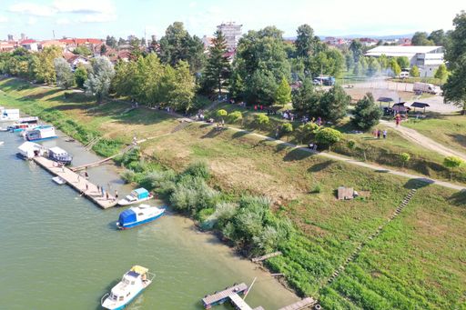 A high angle shot of boats on the water near a grassy hill with people walking in the park at daytime in Bosnia and Herzegovina