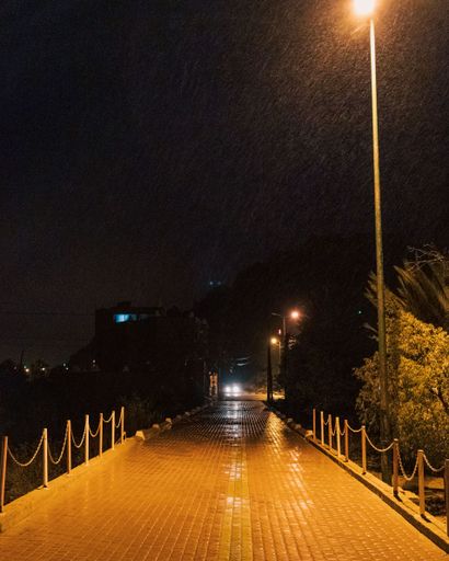 A vertical shot of the pavement illuminated by yellow street lamps at night.