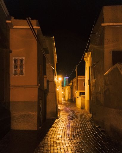 A vertical shot of the illuminated narrow pavement surrounded by buildings at night.