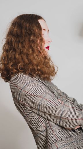 A slow shutter speed shot of an elegant curly girl with a classic gray blazer and red lipstick moving head on a gray background
