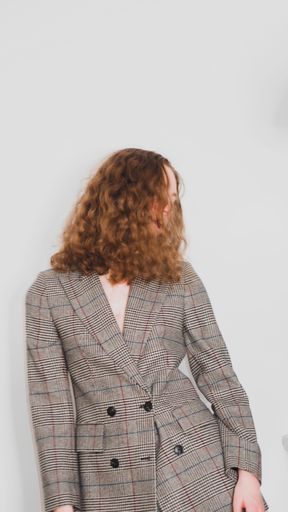 A Slow shutter speed shot of a curly girl with a classic gray blazer moving head on a gray background
