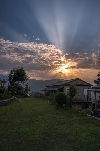 A vertical shot of rural houses on grass meadows and Sunshine over mountains with a cloudy sky