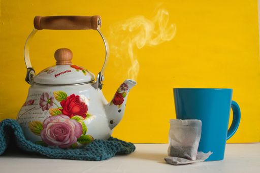 A closeup shot of a colorful tea kettle and a blue tea cup with tea bags on a table