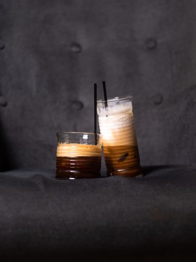 A vertical shot of two glasses of iced coffees with tubule put on a gray sofa