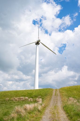 A vertical of a giant wind turbine on the grassy hill in the countryside