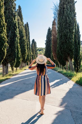 A rear view of woman in sun dress standing on road through landscape in Tuscany