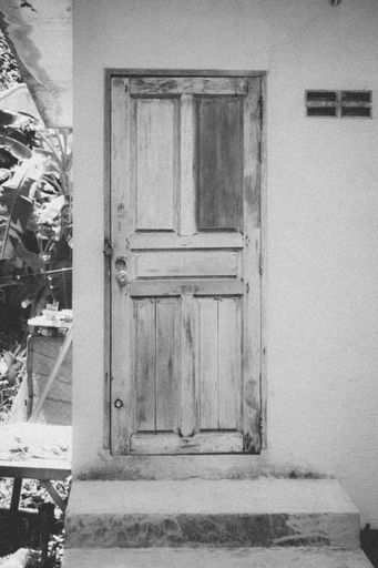 A vertical grayscale shot of a part of a building with an old wooden door.