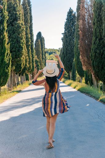 Rear view of woman in sun dress standing on road through landscape in Tuscany