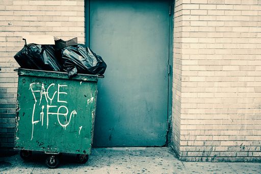 A green trash can in front of the door with Face Life writing on it