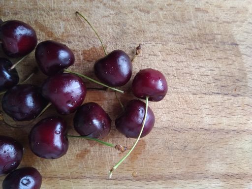 A high angle shot of fresh cherries on a wooden board under the lights