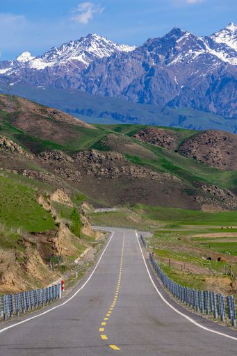 A vertical shot of an empty road passing through mountains on a sunny day
