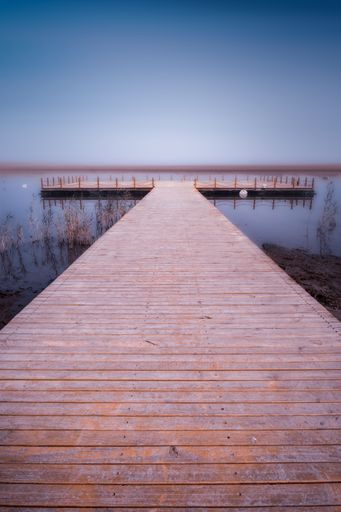 A vertical shot of a wooden pier in a lake during sunset
