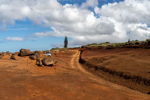 A white Jeep parked at Garden of the Gods on Lanai, Hawaii, next to the Polihua Trail, a volcanic red dirt road.