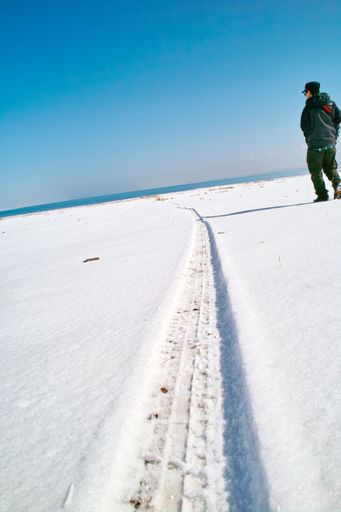 A snowy field with the trace of a ski and a person walking on the snow under a clear cloudless sky