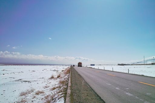 An Asphalt road passing through a snowy field with a truck coming from afar