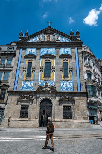 A man walking outside an old church in Porto, Portugal under a clear sky