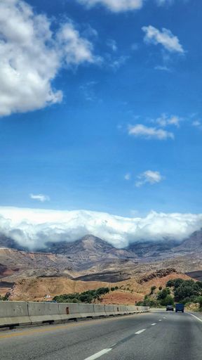 A vertical shot of a road with mountains in the background under a cloudy sky