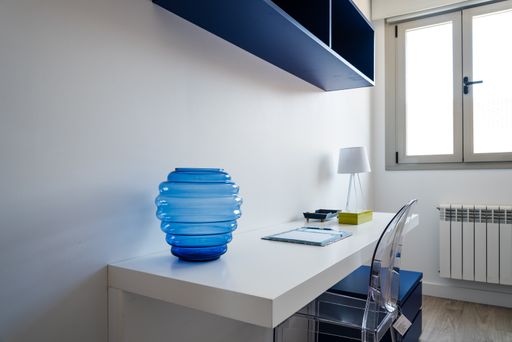 A minimalistic room with a white table, blue shelves and a bedside table