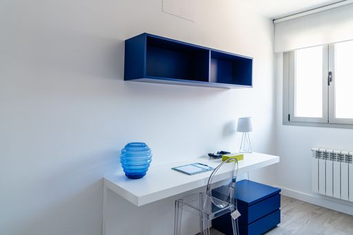 A minimalistic room with a white table, blue shelves and a bedside table