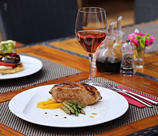 A closeup of roasted meat with asparagus in a plate on the table with drinks and spices on it