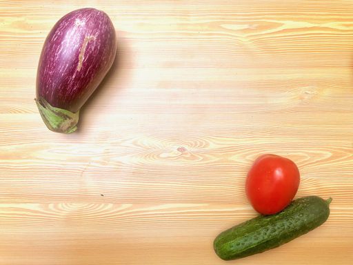 A high angle shot of a tomato, cucumber, and an eggplant on a wooden surface