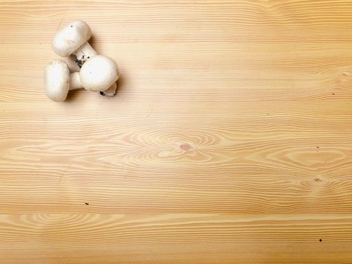 A high angle shot of three small mushrooms on a wooden surface