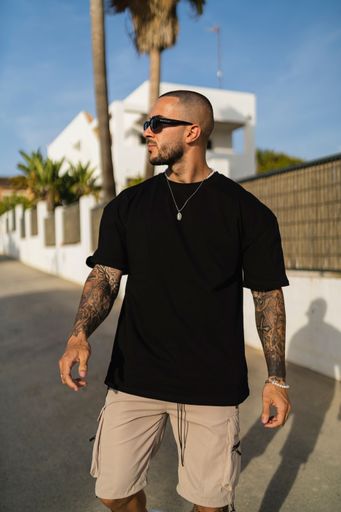 A vertical shot of a young tattooed man wearing a black t-shirt and beige shorts