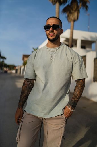 A vertical shot of a young tattooed man wearing a green t-shirt and shorts